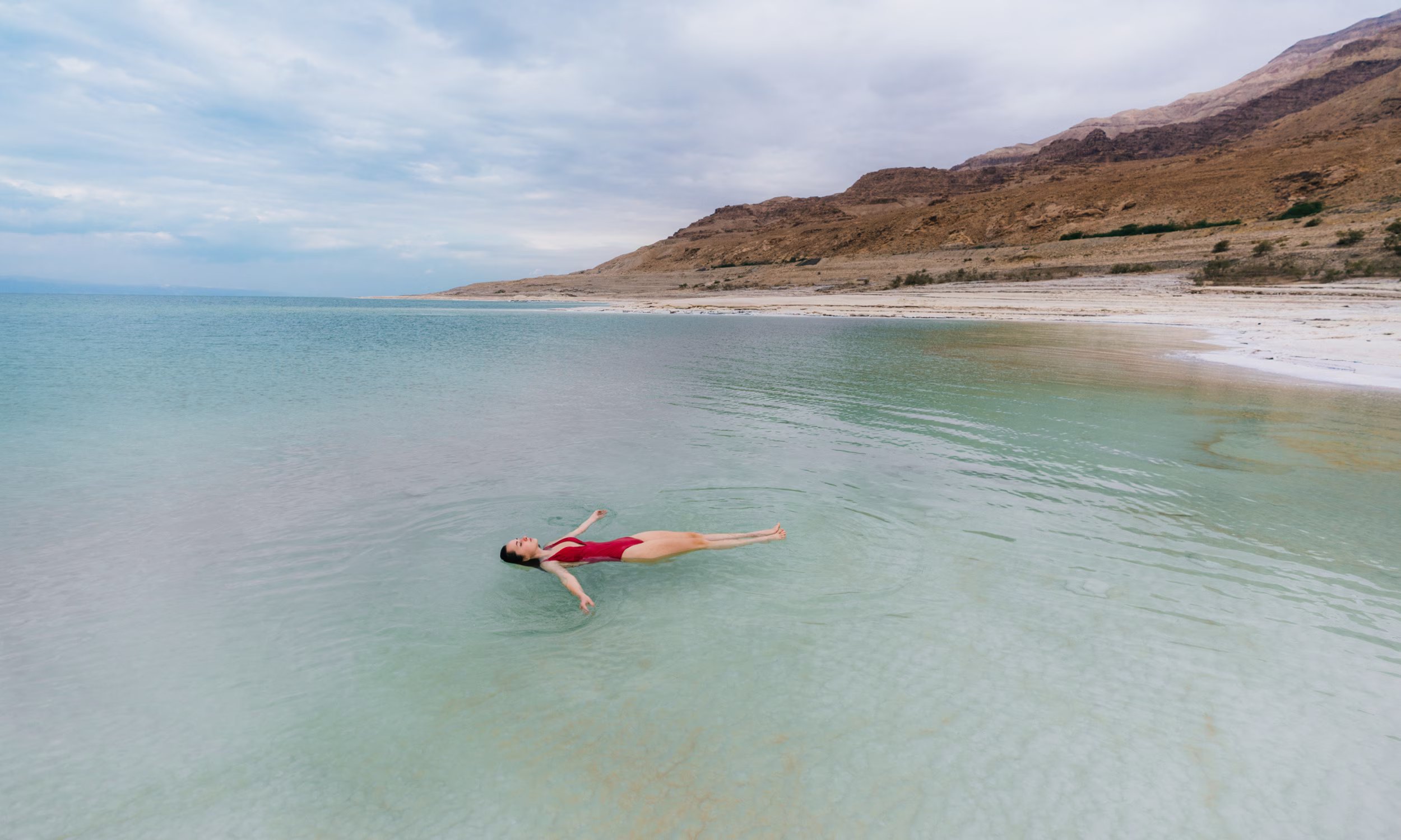 Person floating on the salty waters of the Dead Sea with desert mountains in the background. 