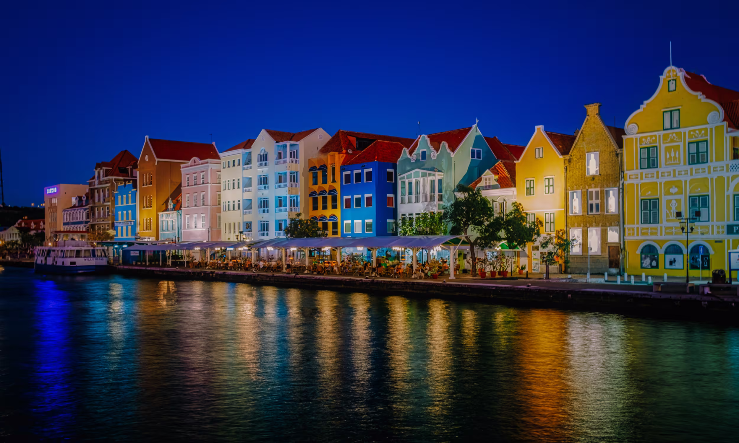 Colorful colonial houses reflected on the water in Willemstad, Curaçao, at night.