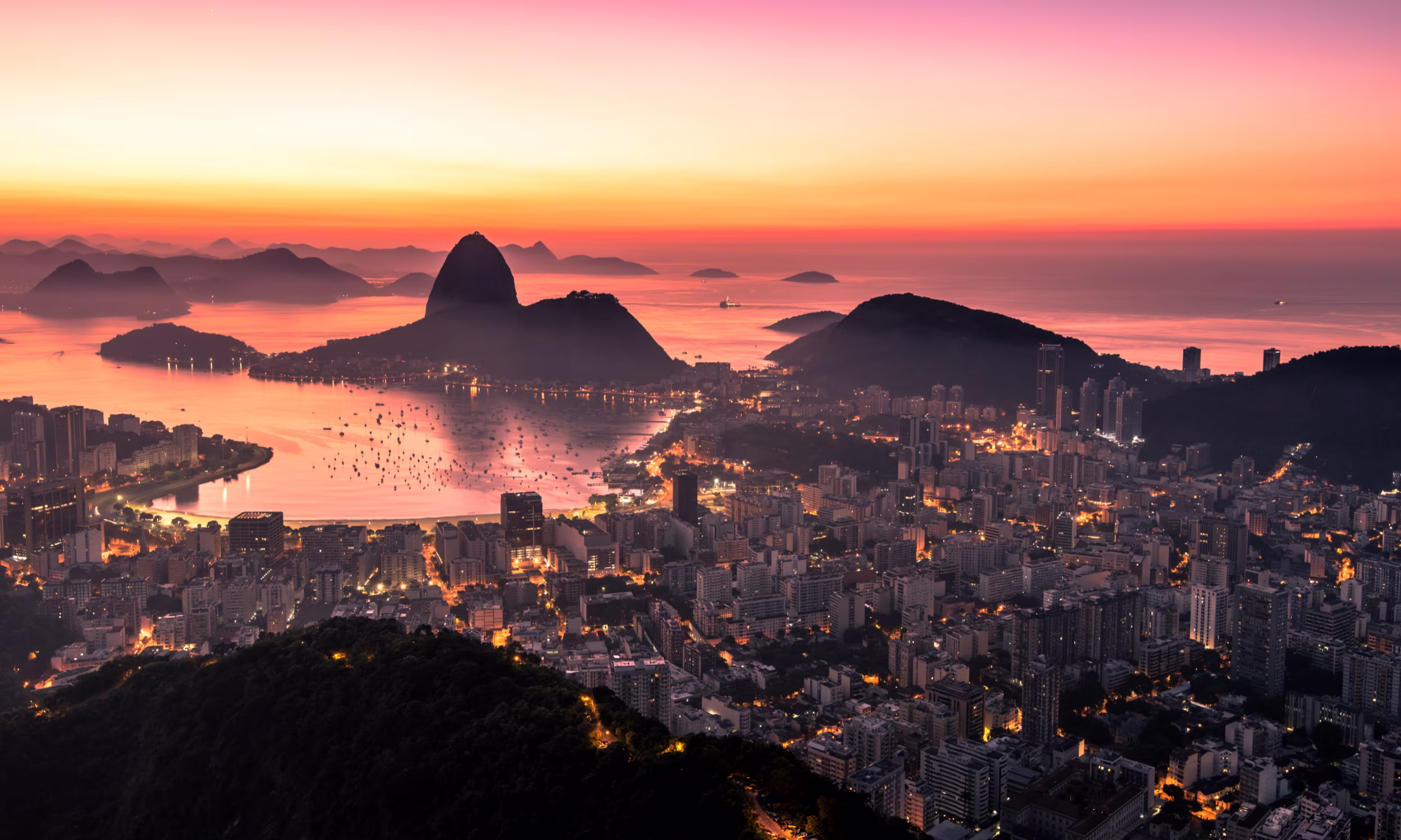 Aerial view of Rio de Janeiro at sunset, with Sugarloaf Mountain and the bay glowing in golden light. 