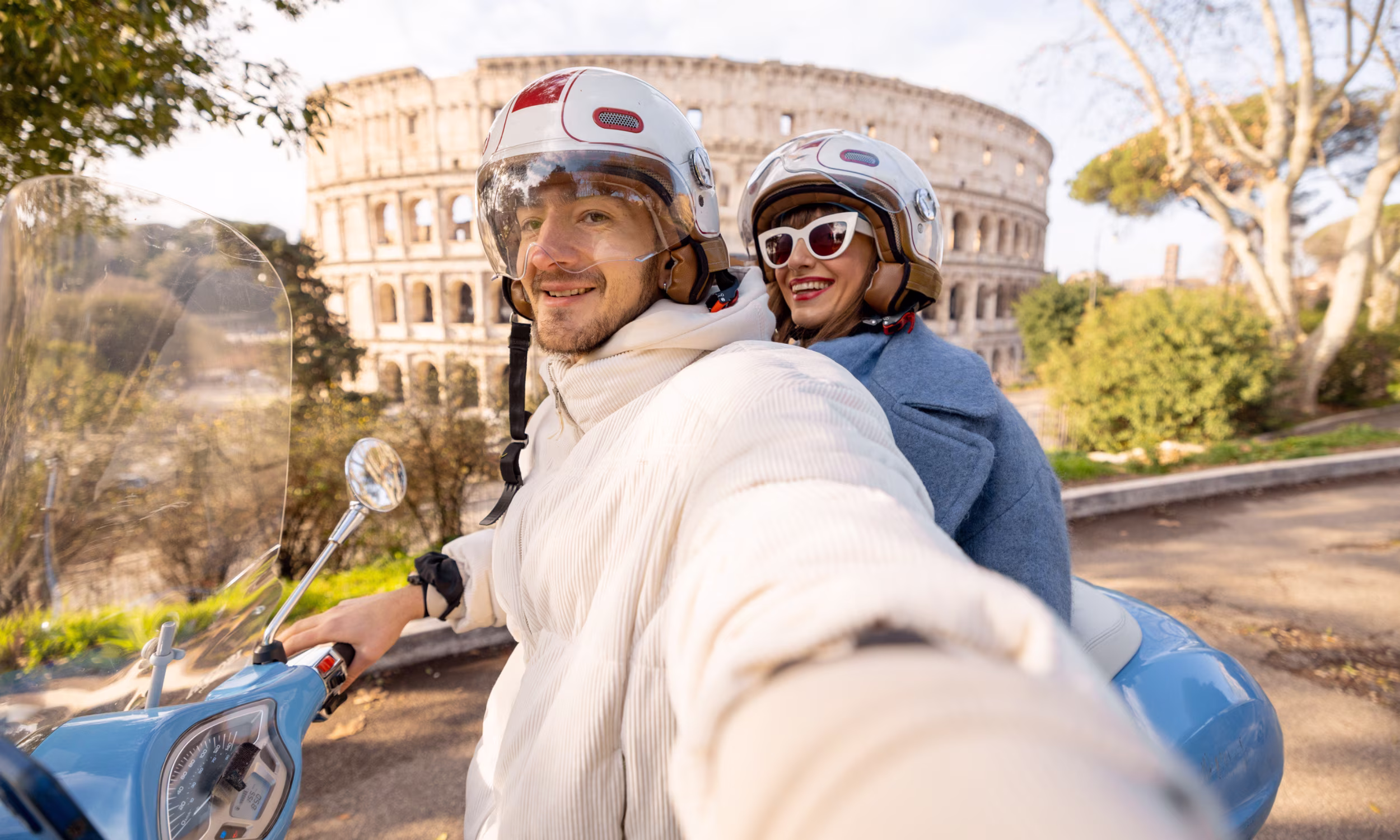 Couple riding a Vespa near the Colosseum in Rome on a sunny day. 