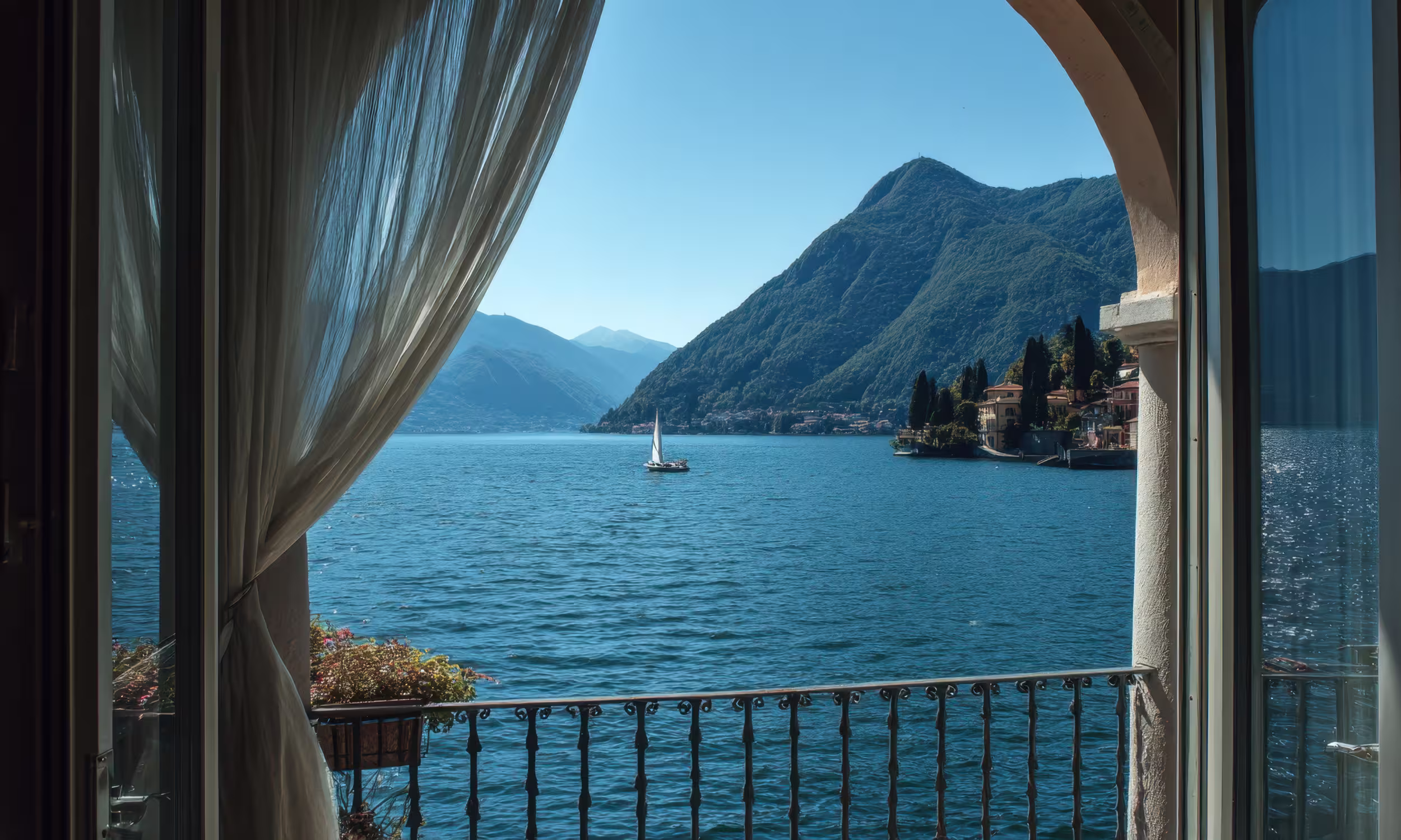View of Lake Como from a hotel balcony, with mountains in the distance and a sailboat on the lake.