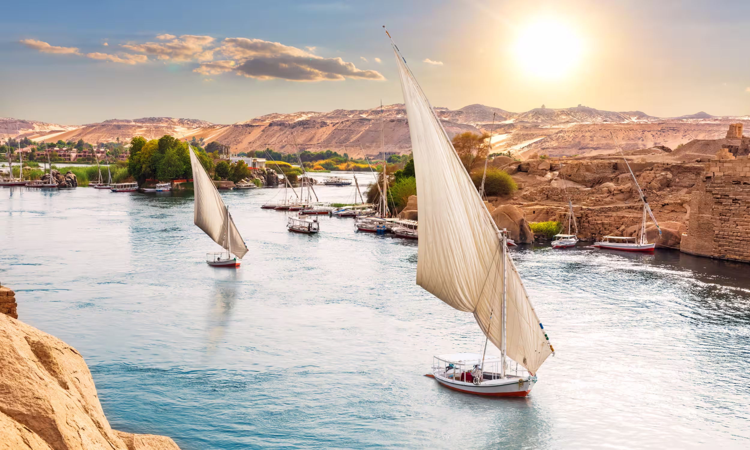 Traditional feluccas sailing on the Nile River in Aswan at sunset. 