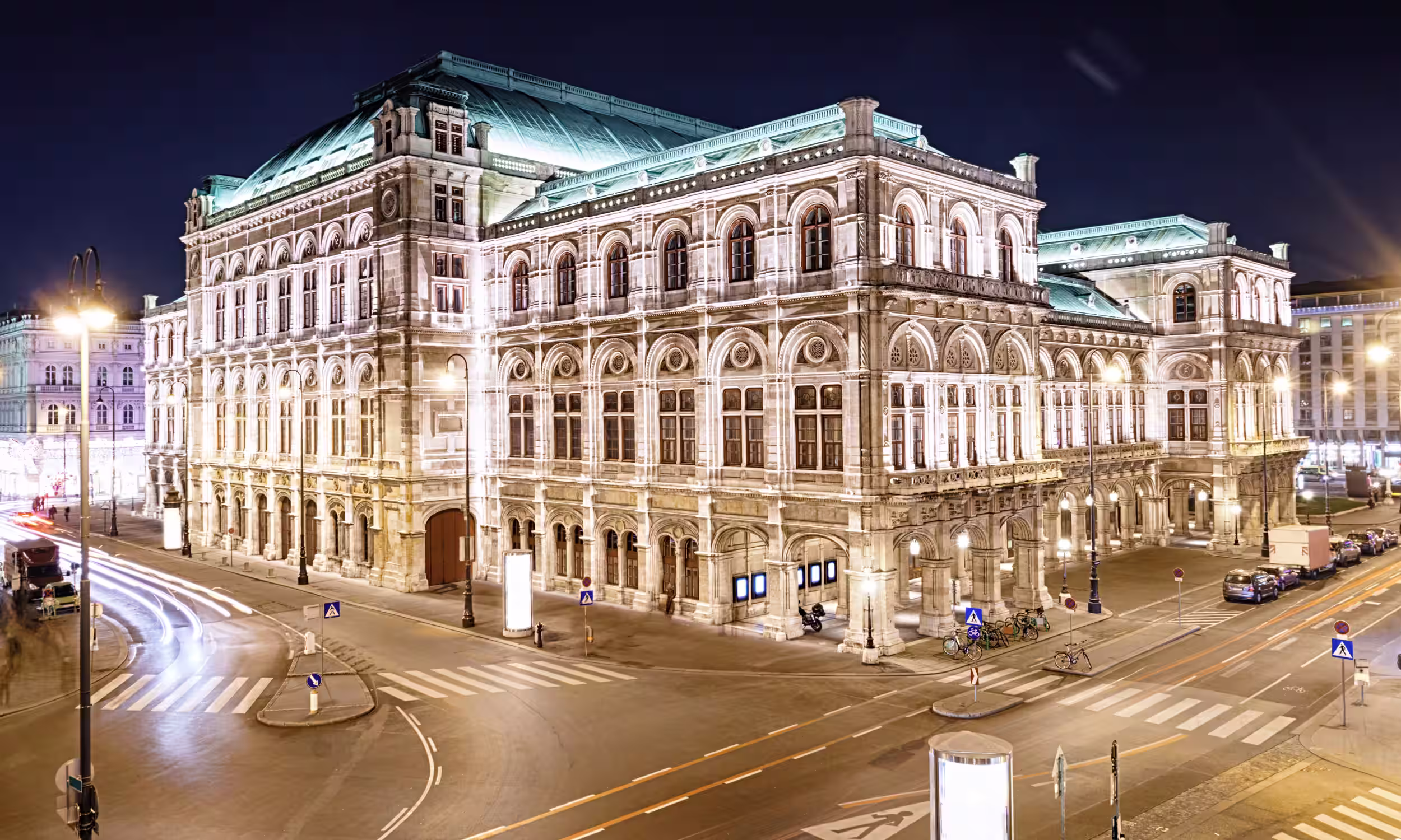 Couple in front of the Vienna State Opera House lit up at night, romantic honeymoon scene.