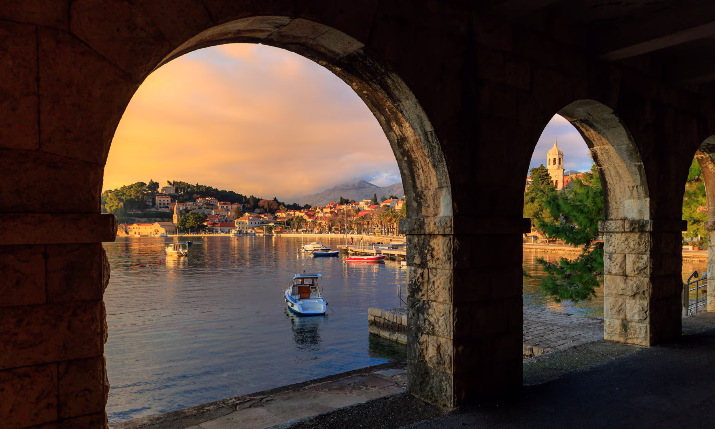 Croatian seaside town at golden hour with stone arch in the foreground. 