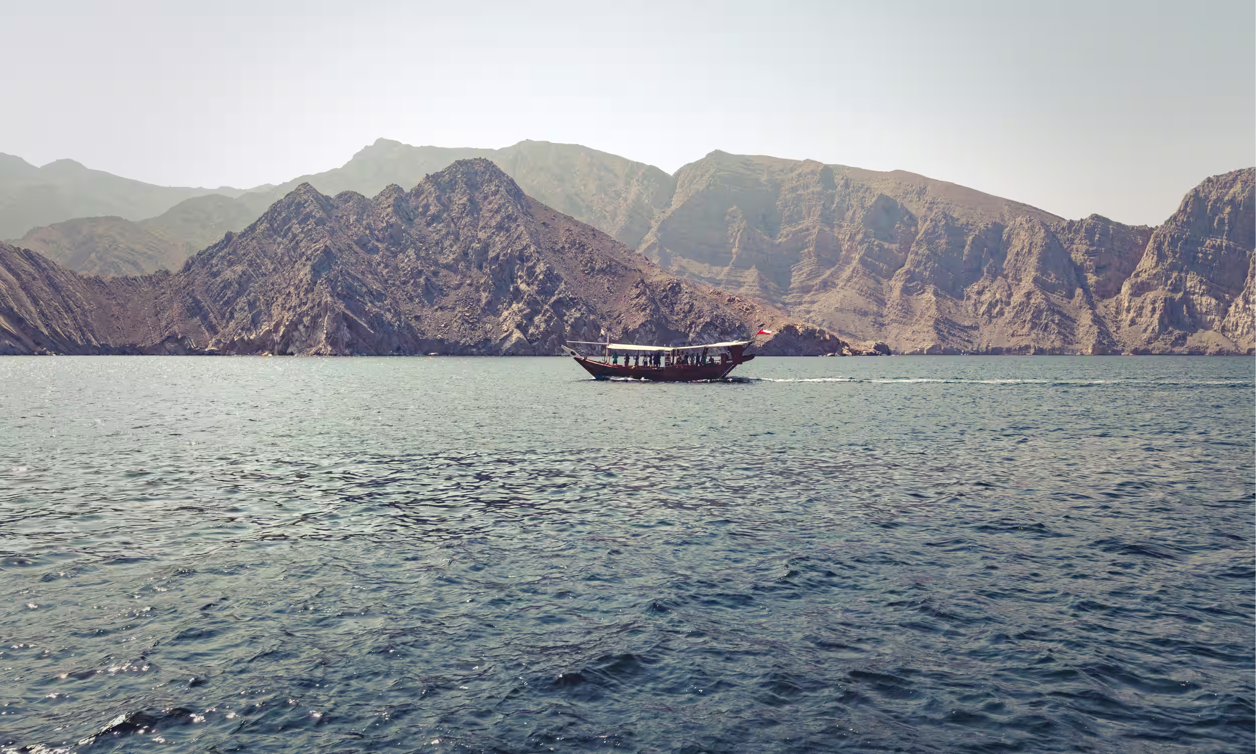 Traditional dhow boat sailing between mountains and sea in Oman. 