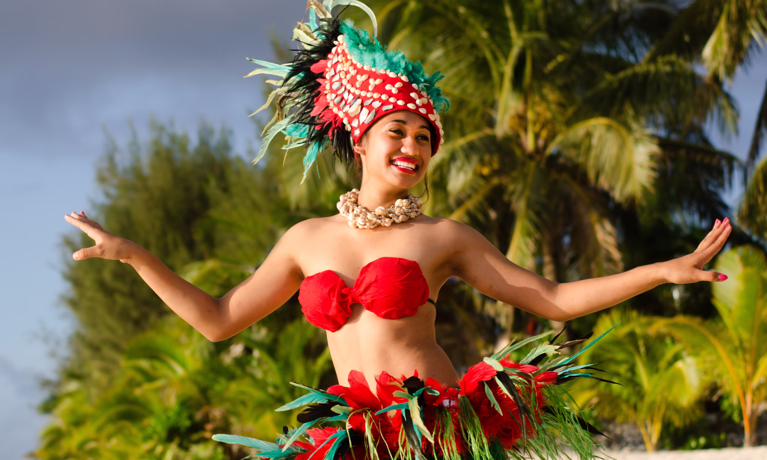 Tahitian dancer in traditional attire performing among palm trees. 