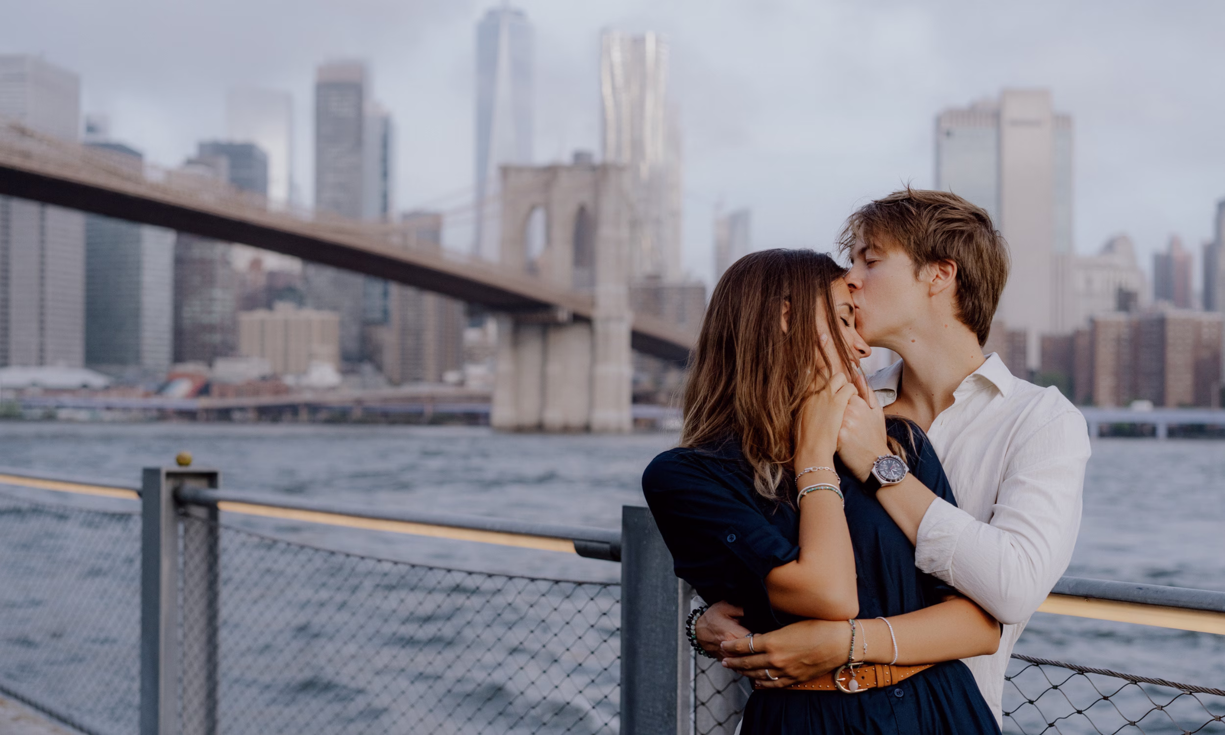 Casal abraçado junto à Ponte de Brooklyn com skyline de Nova Iorque, lua de mel romântica 