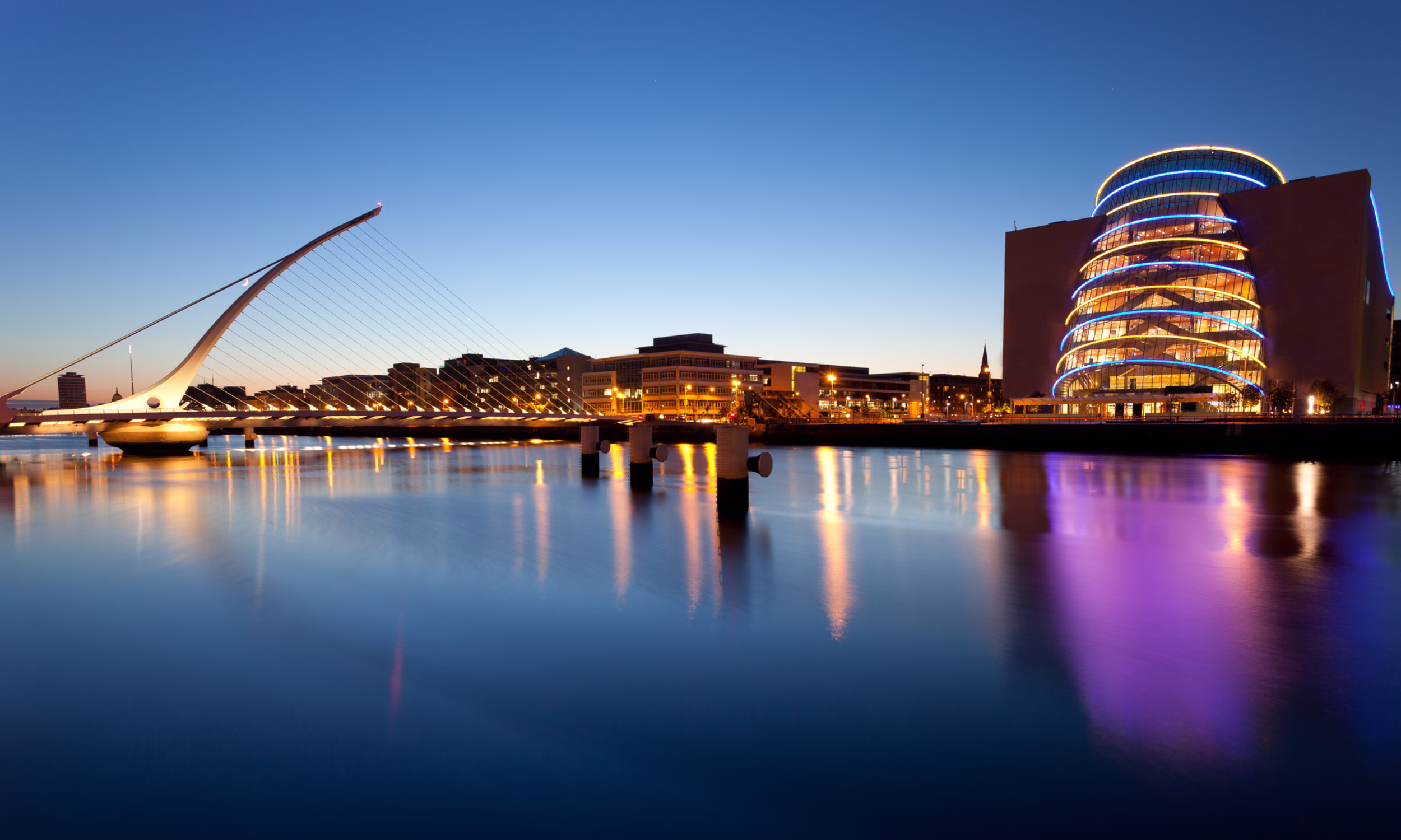 Vista noturna de Dublin com edifícios iluminados junto ao rio.