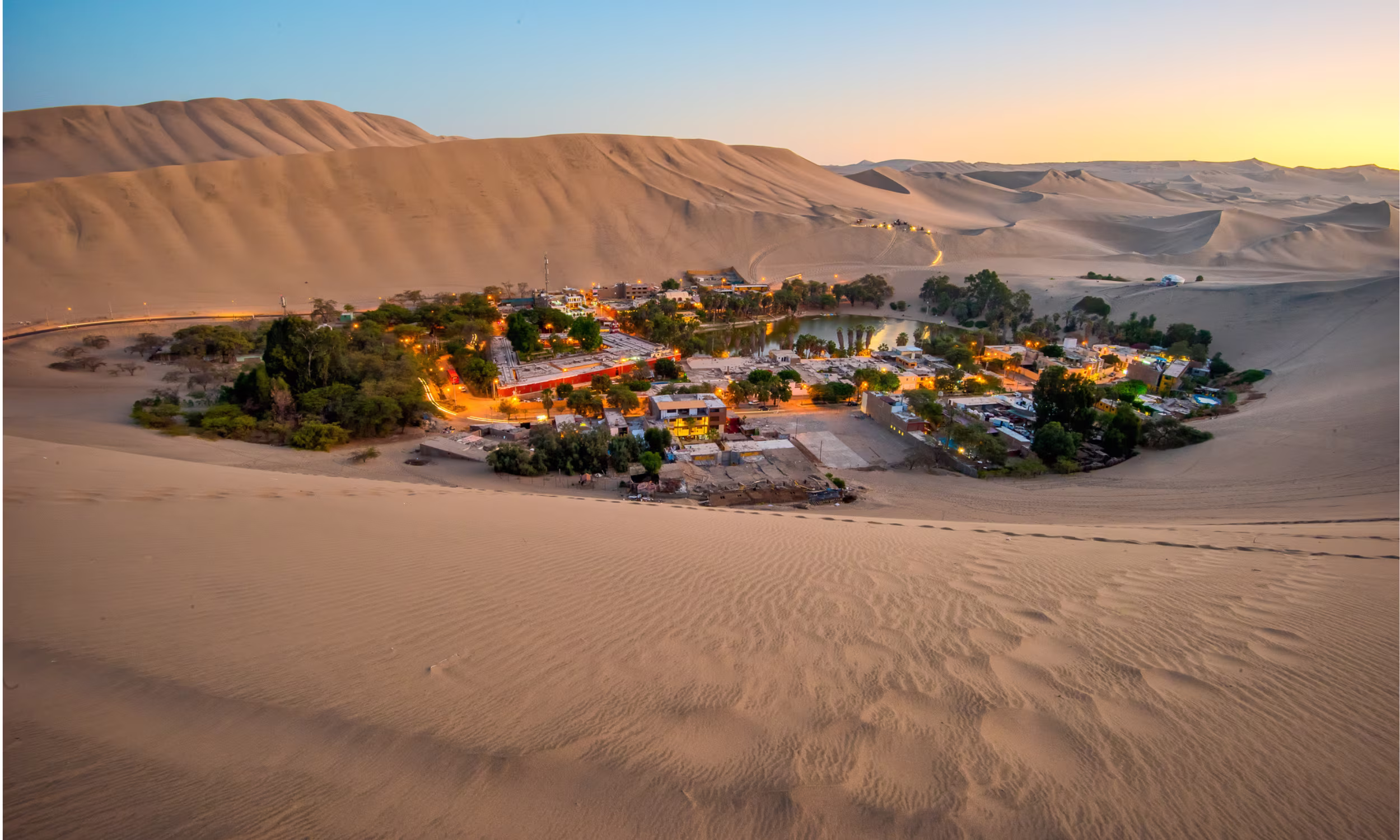Sand dunes in the Peruvian desert with a small settlement in the distance.
