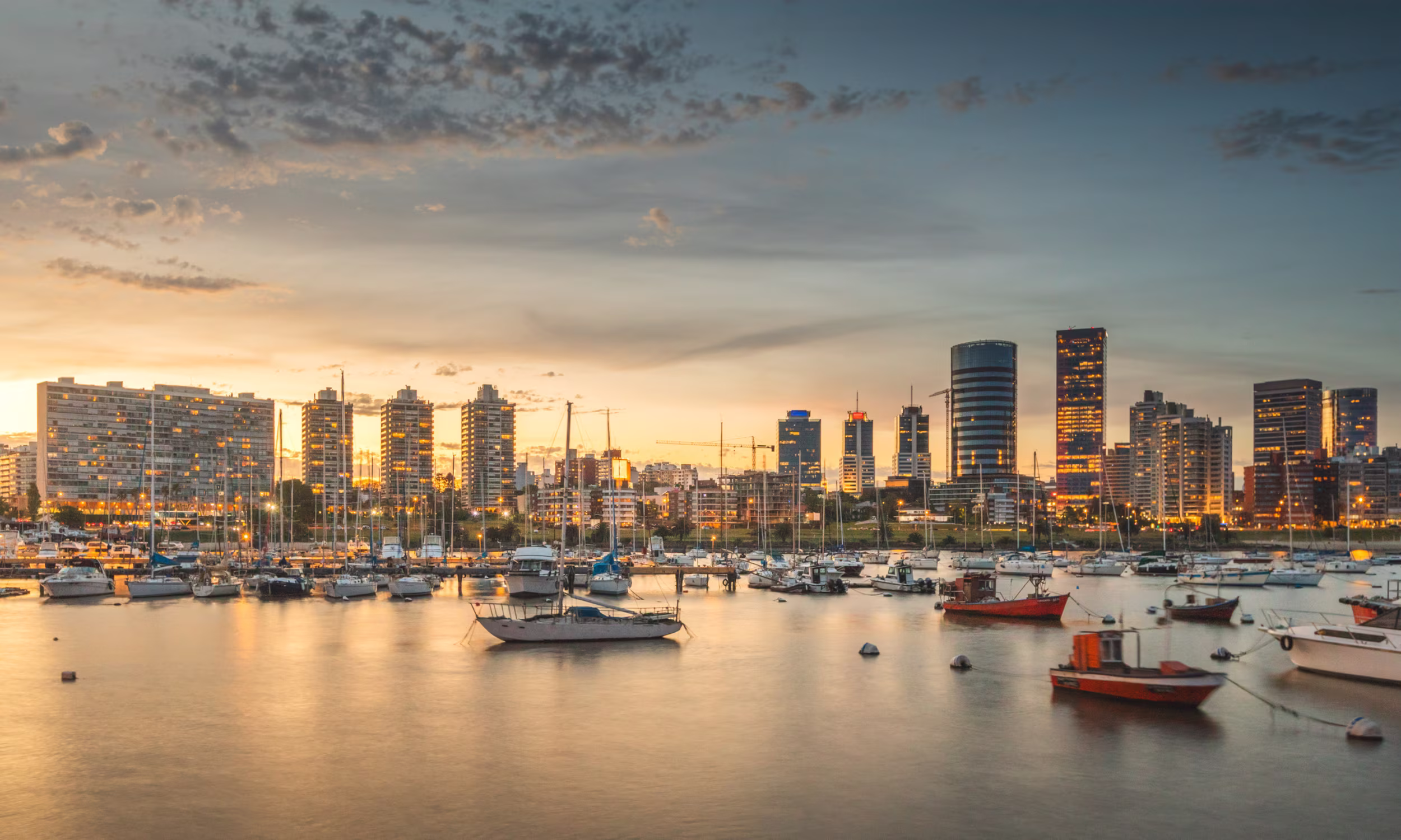 Montevideo skyline at sunset with buildings reflected on the water.
