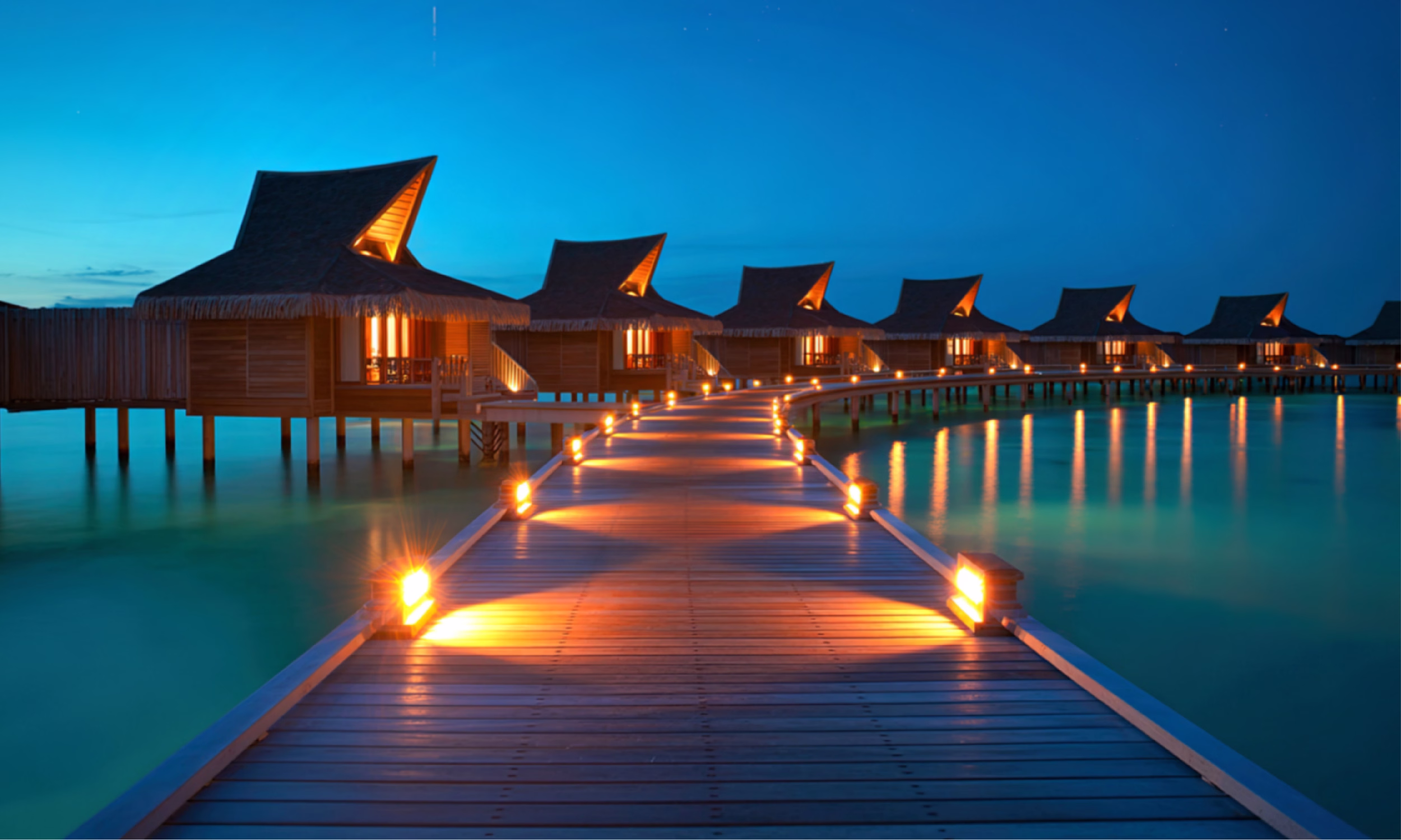Overwater bungalows lit at night in a tropical luxury resort