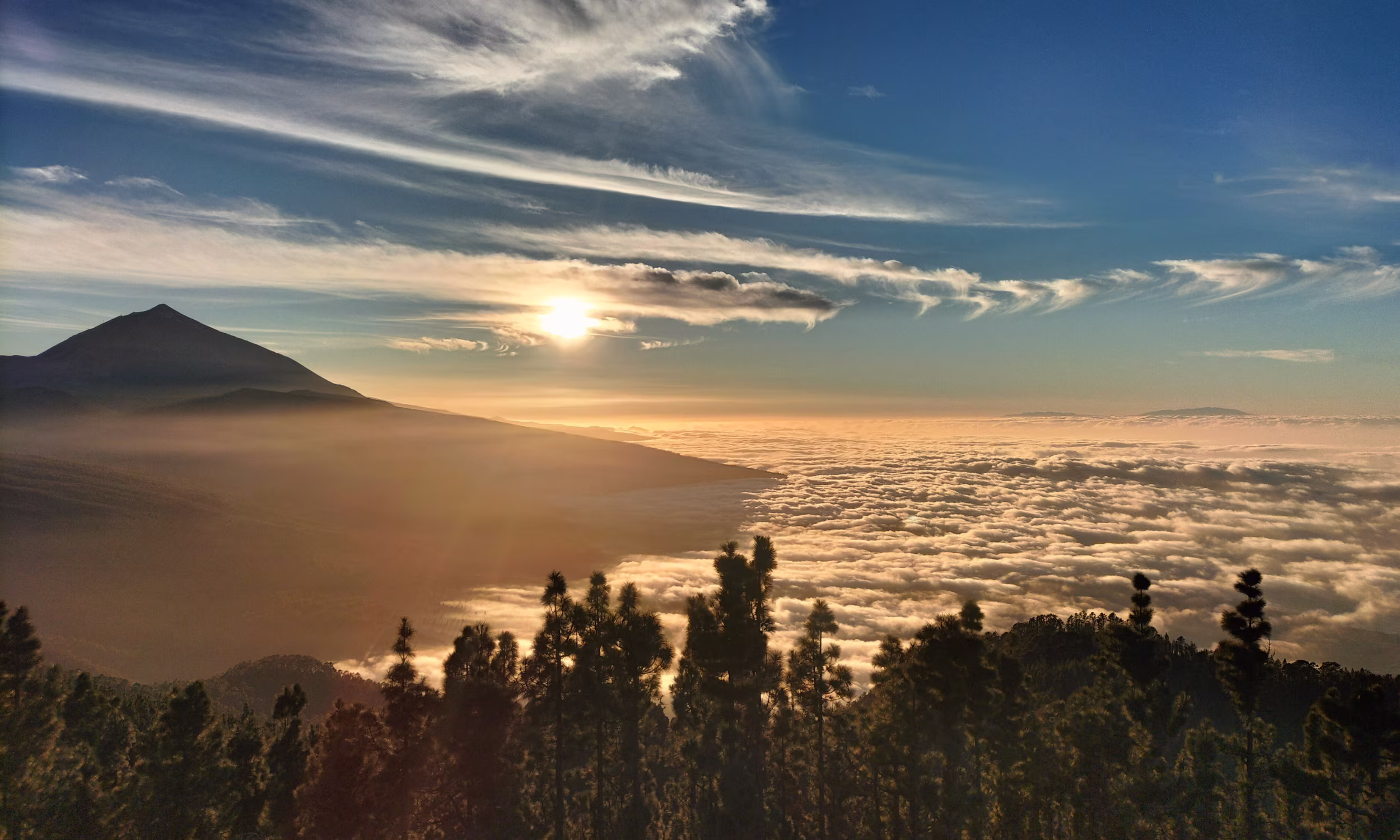 Pôr do sol sobre uma paisagem vulcânica nas Ilhas Canárias, com luz quente e vista ampla sobre montanhas.