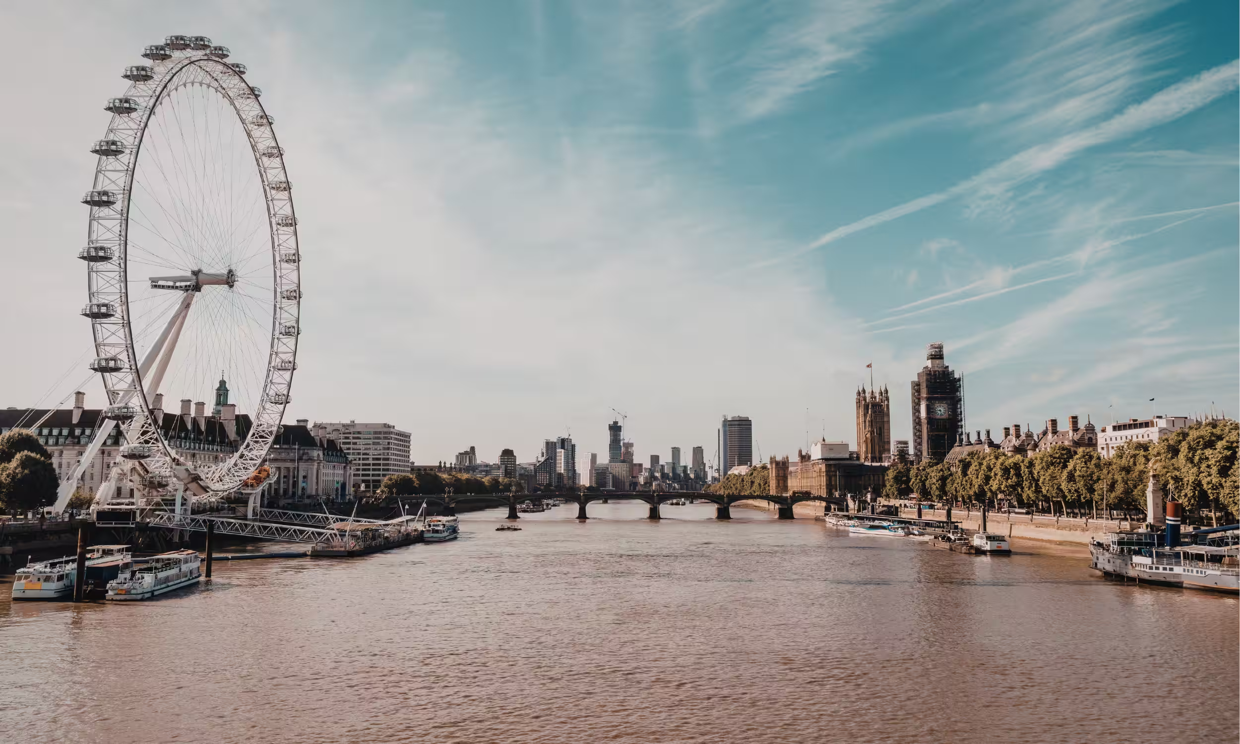 Skyline de Londres com o London Eye e o rio Tamisa sob um céu suave.