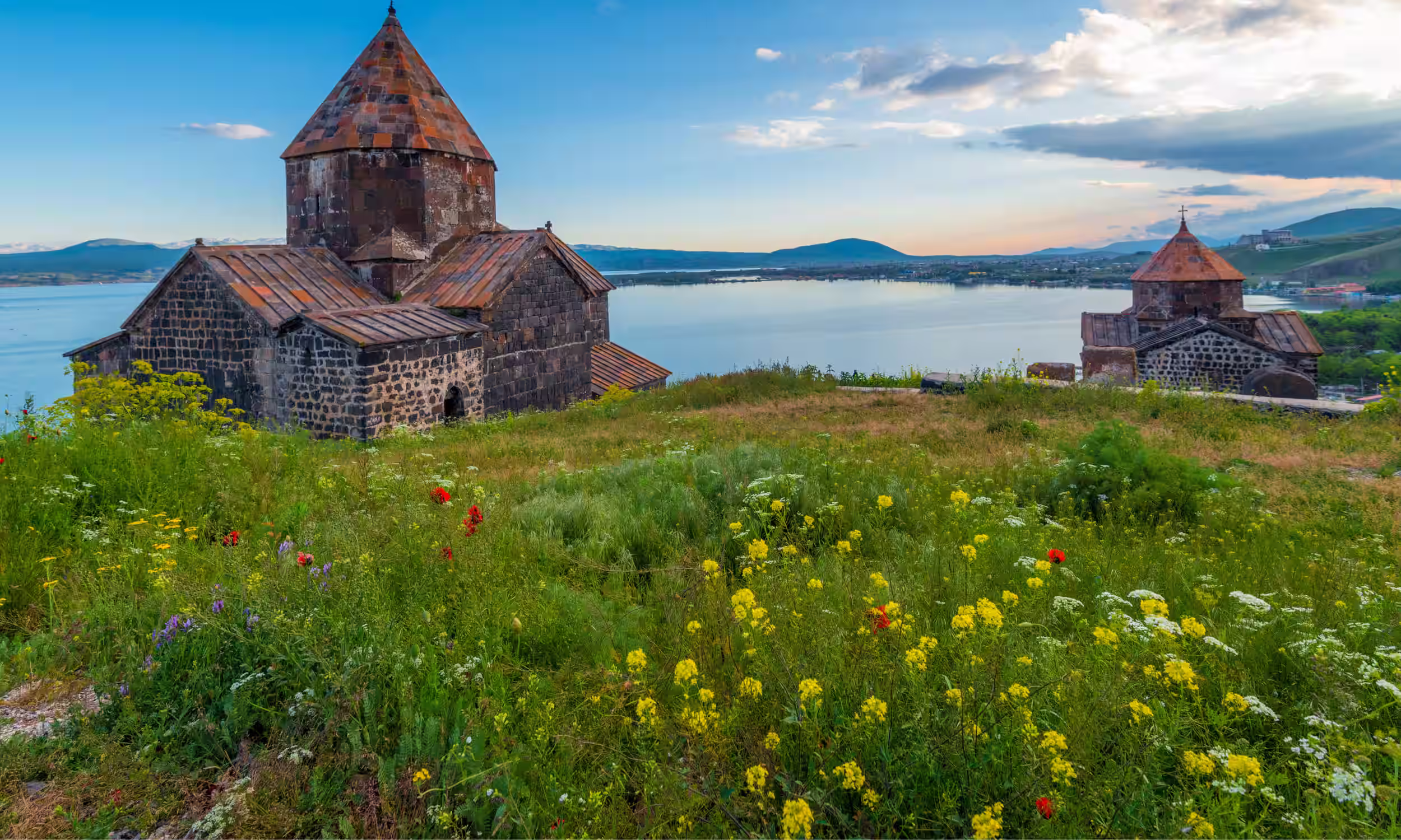 Mosteiro de Sevanavank ao pôr do sol sobre o Lago Sevan, com luz dourada refletida na água.
