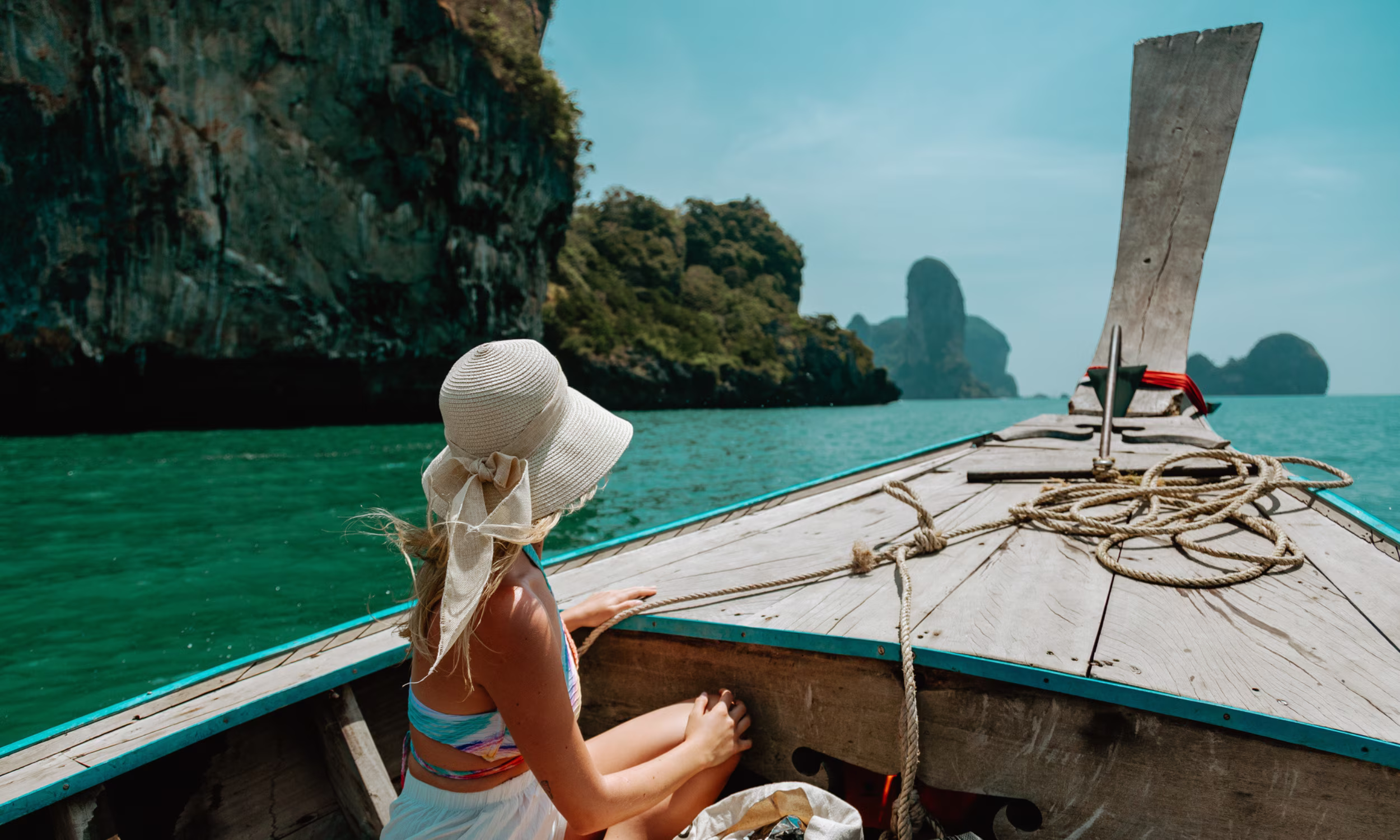 Mulher num barco tradicional tailandês entre falésias tropicais durante uma viagem de lua de mel na Tailândia.