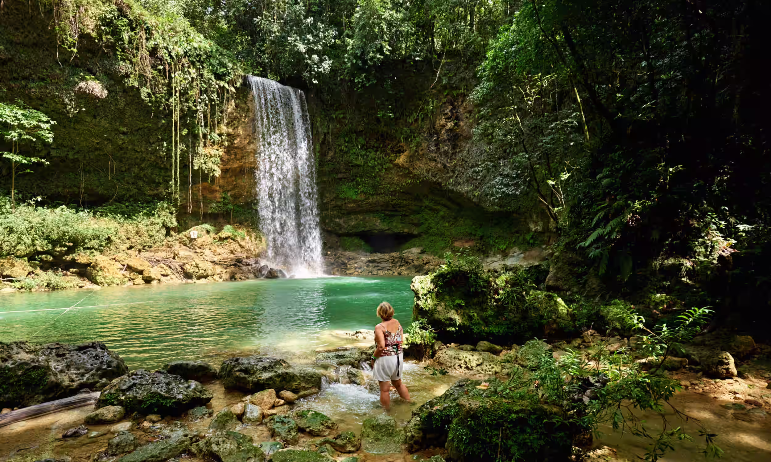 Woman admiring a waterfall formed by the Socoa River surrounded by tropical rainforest in the Dominican Republic.