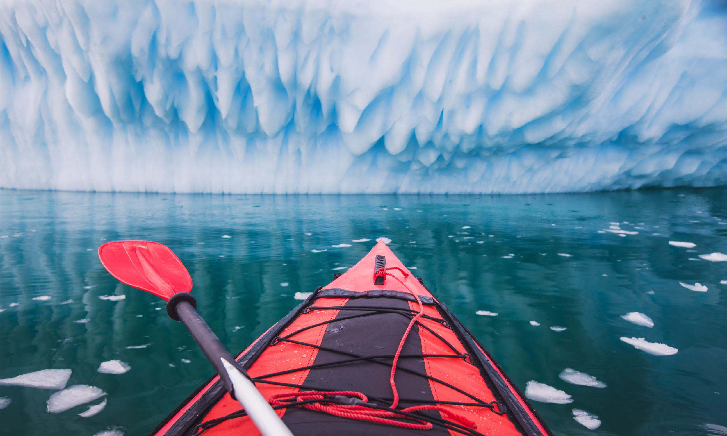 Caiaque vermelho a navegar junto a icebergs nas águas da Antártica.