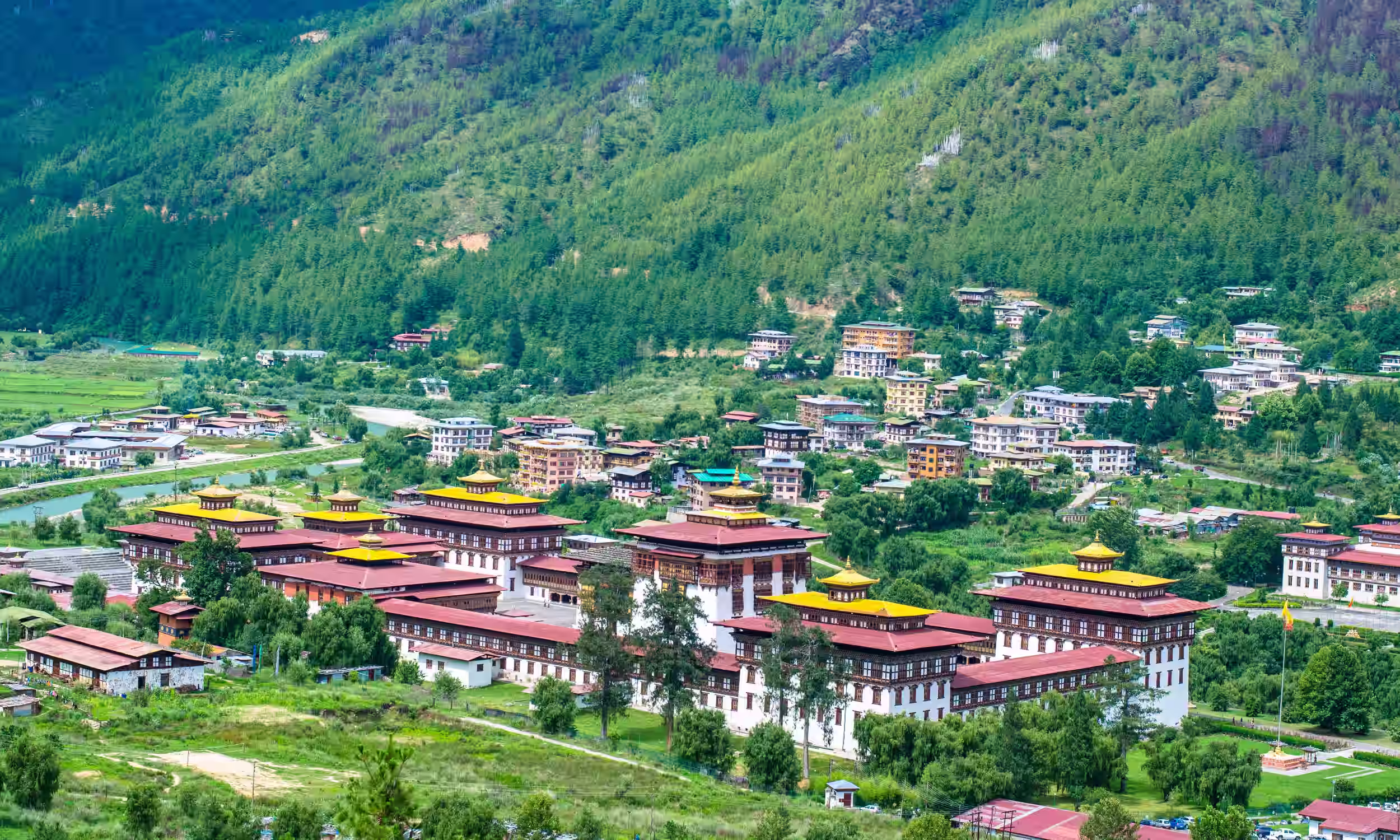 Vista aérea de um dzong em Thimphu, rodeado pelas montanhas e pela paisagem verde do Butão.