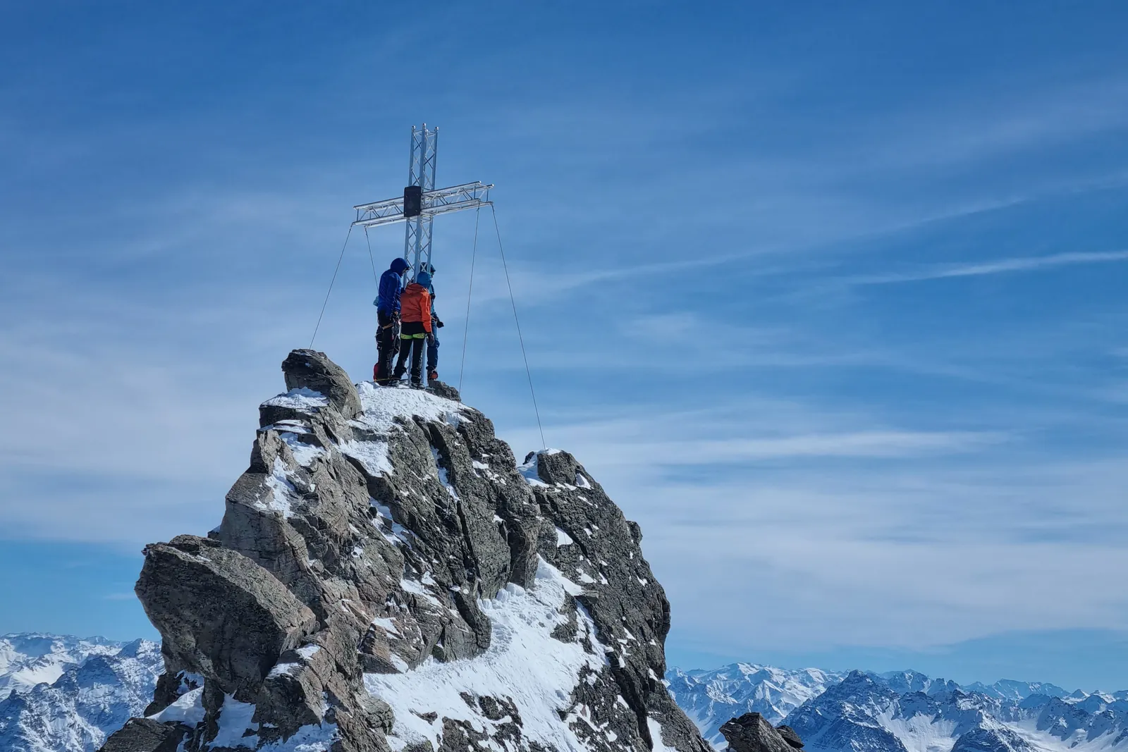 Two climbers at a summit cross on a rocky alpine peak above the clouds