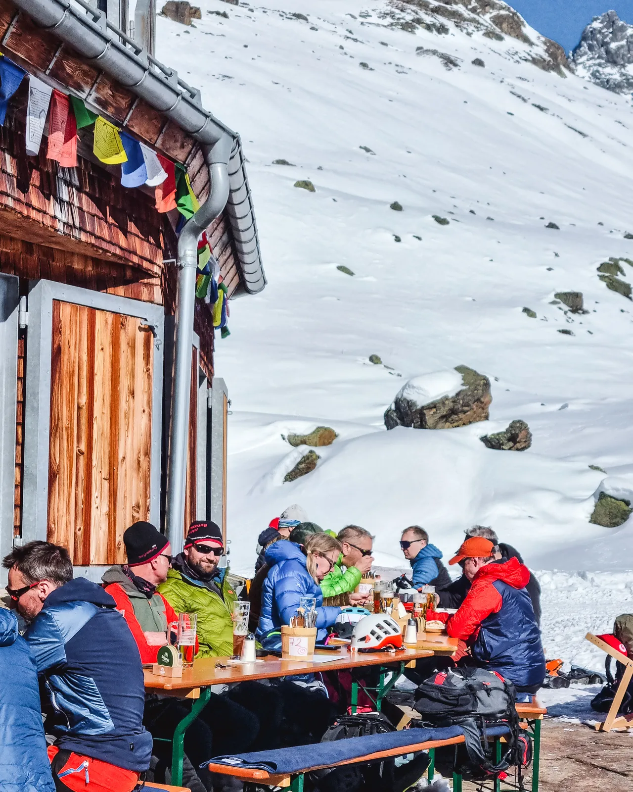 Ski tourers having lunch on a sunny hut terrace surrounded by snowy mountains