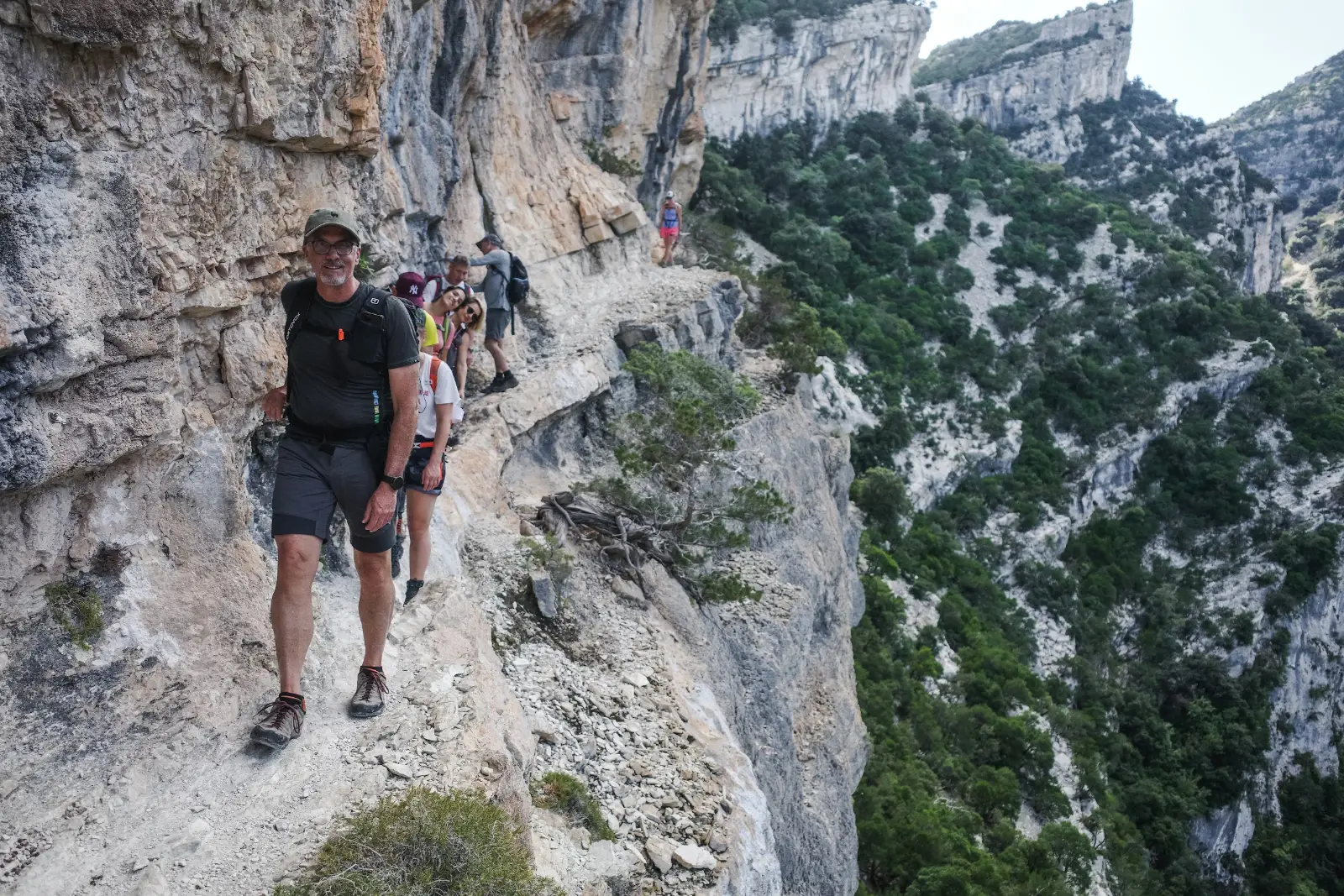 Trekkers walking a narrow limestone ledge above a forested gorge