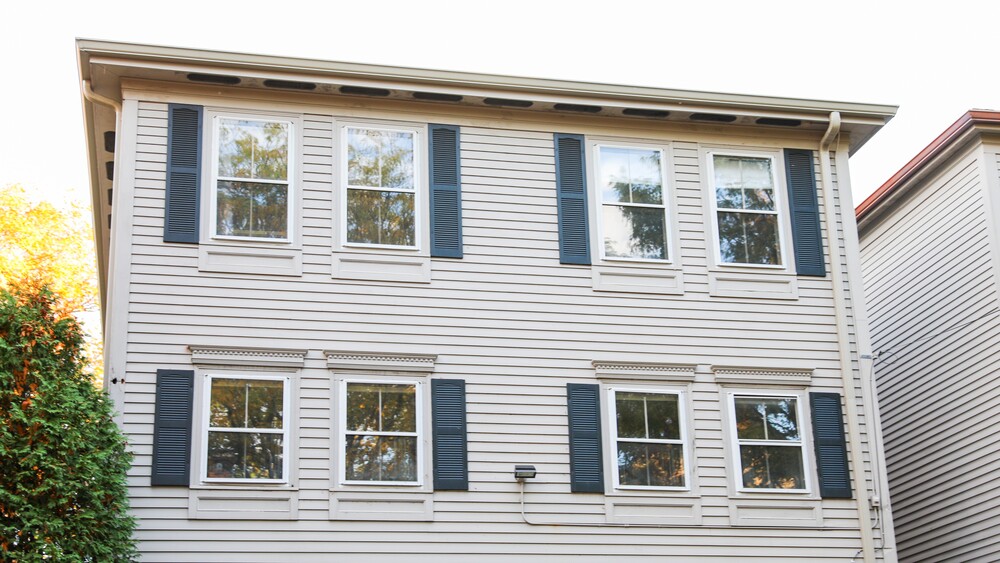 Two-story home with white siding and white framed replacement windows with blue shutters