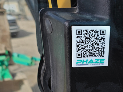 QR code sticker with the text PHAZE CONCRETE on a black metal surface outdoors.