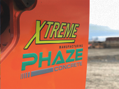 Close-up of orange equipment with XTREME Manufacturing Phaze Concrete logo outdoors.
