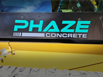 Close-up of machinery with Phaze Concrete logo in turquoise and gray on a black and yellow surface.