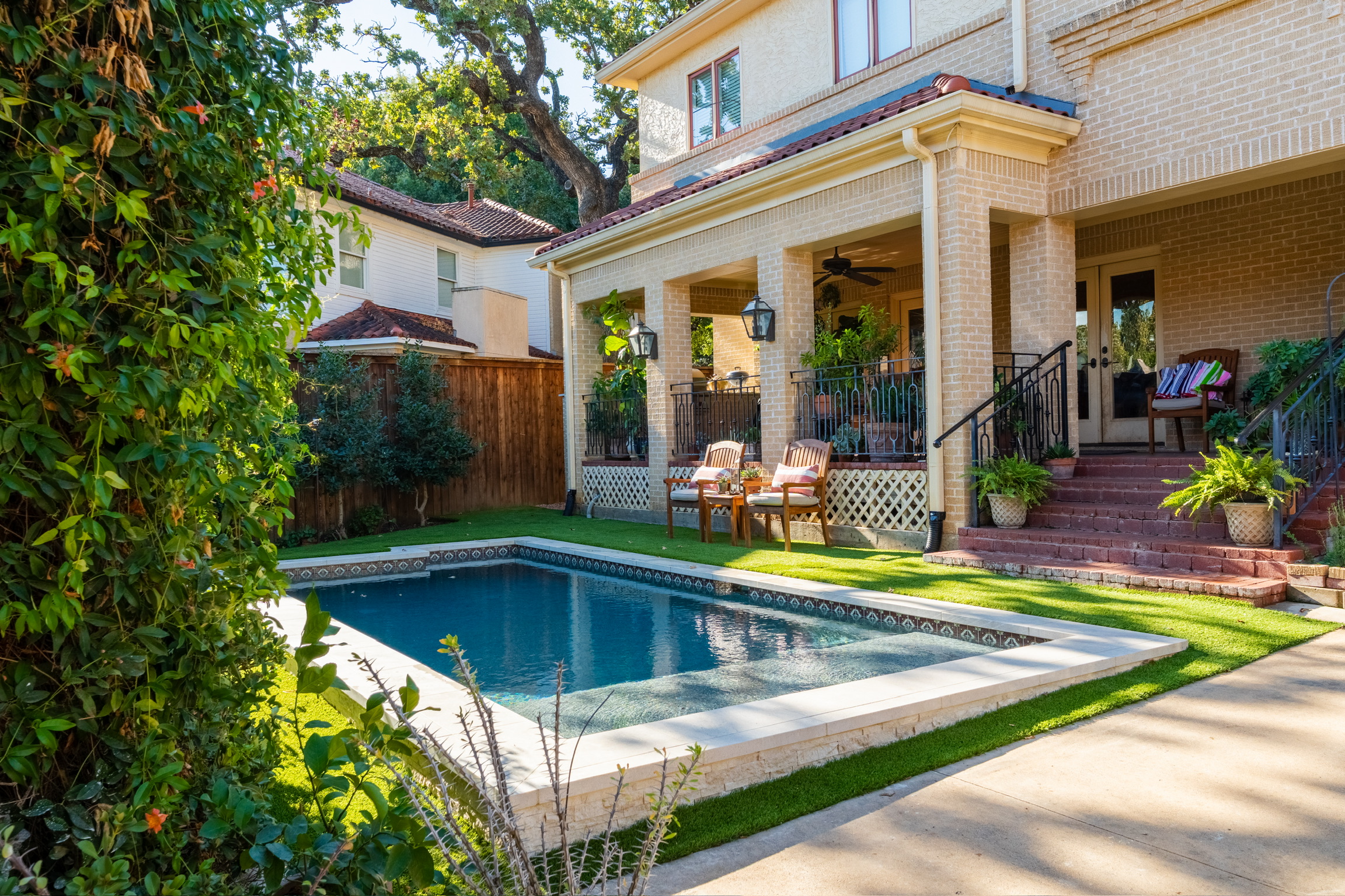 Finished custom pool with stone coping and turf beside a covered porch