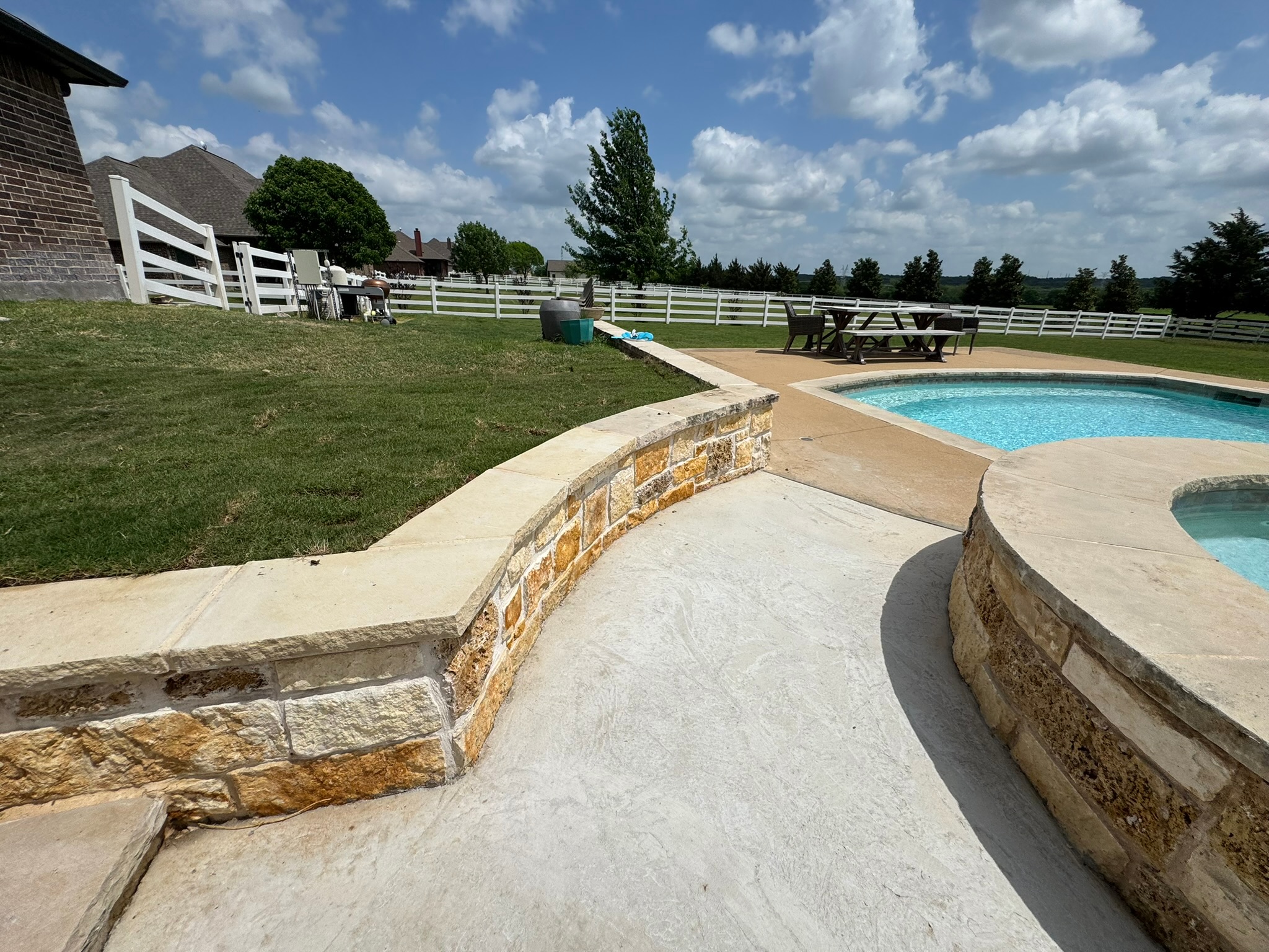 Curved stone retaining wall with new coping beside the spa