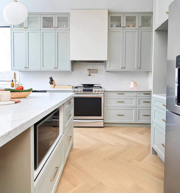 Sage green shaker kitchen with white counters and herringbone floor