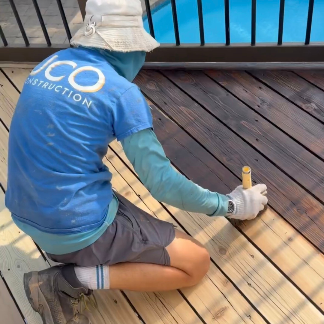UCO Construction group worker stains a deck with a brush