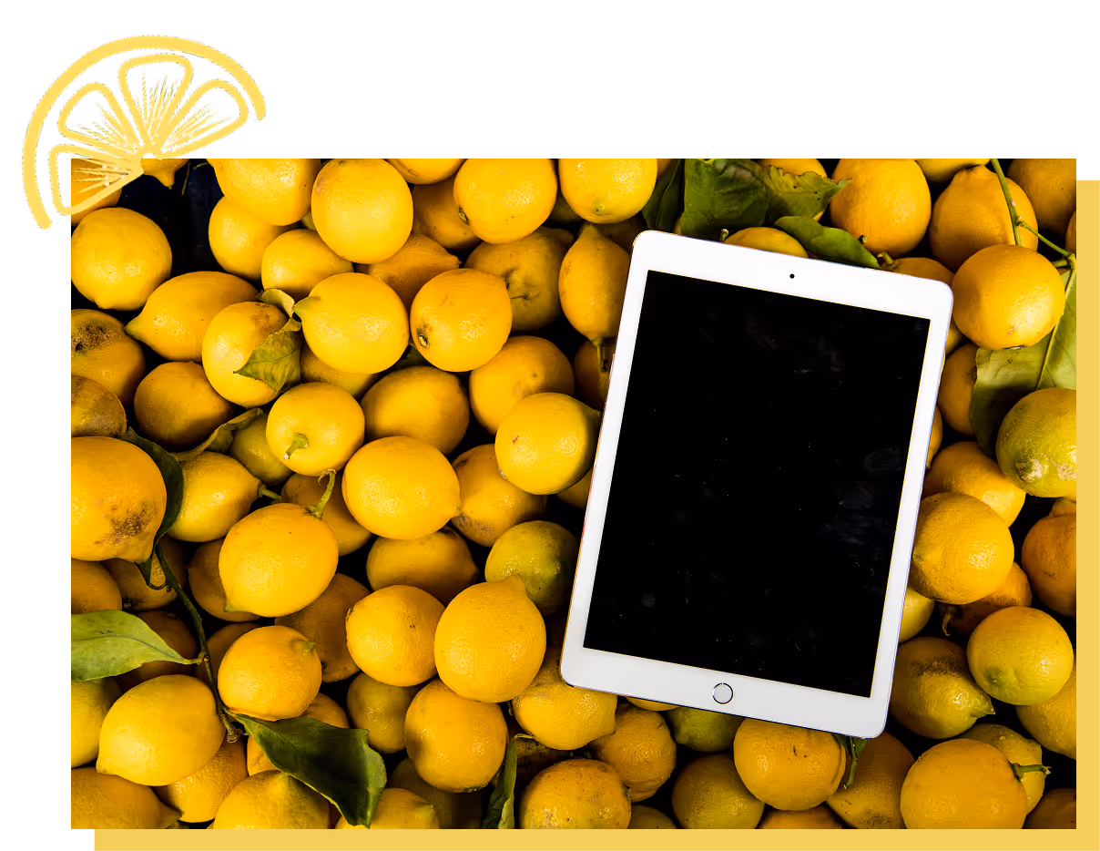 White tablet with black screen placed on a pile of fresh yellow lemons with green leaves.