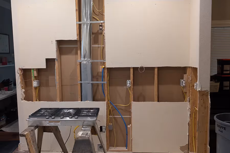 Open kitchen walls during rough-in phase showing plumbing and electrical work in progress