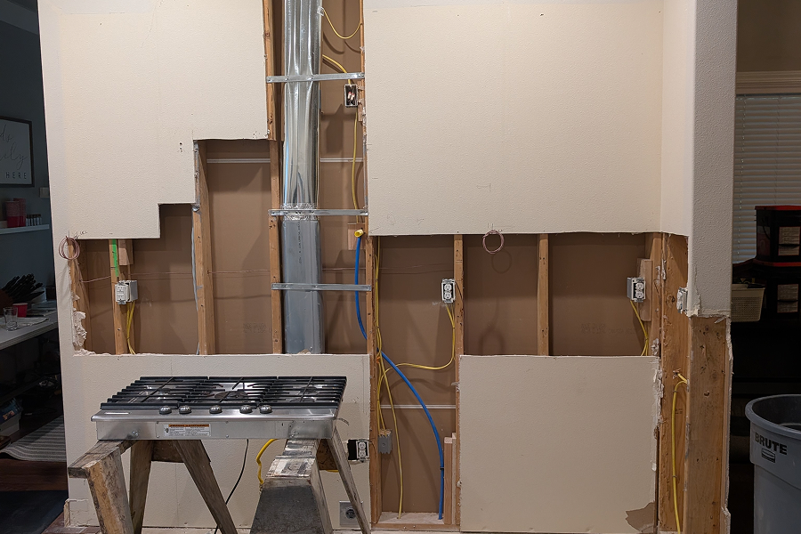 Open kitchen walls during rough-in phase showing plumbing and electrical work in progress