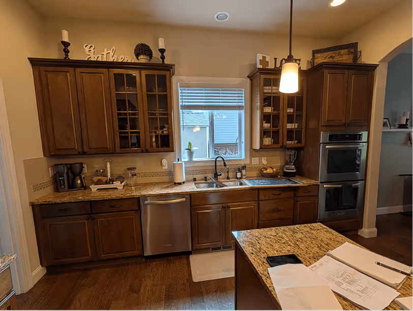 Sink wall with dark upper cabinets, double wall ovens, and a pendant light hanging over the peninsula