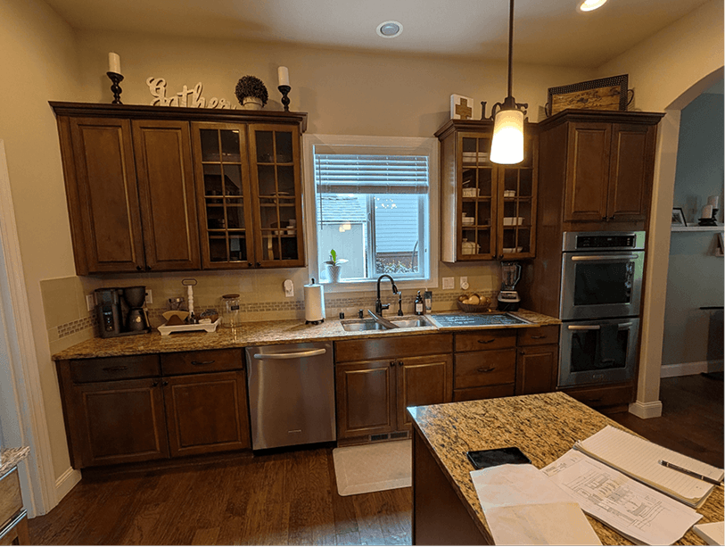 Sink wall with dark upper cabinets, double wall ovens, and a pendant light hanging over the peninsula