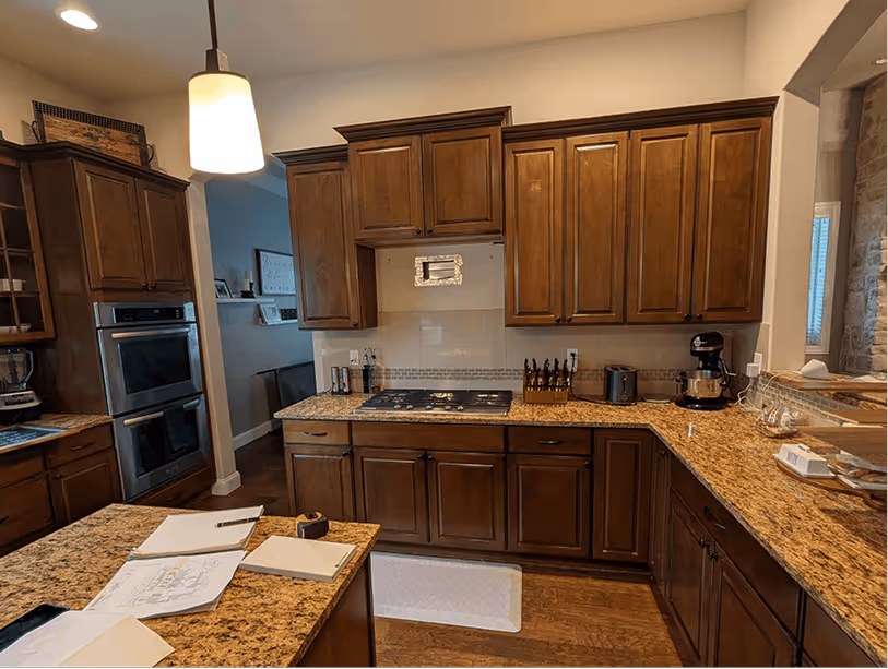 Cooking wall showing gas cooktop dropped into dark granite counter with double wall ovens on the right