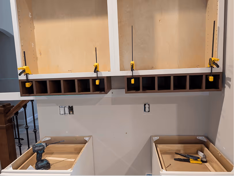 Upper cabinets clamped into place with yellow bar clamps holding a full row while fasteners set