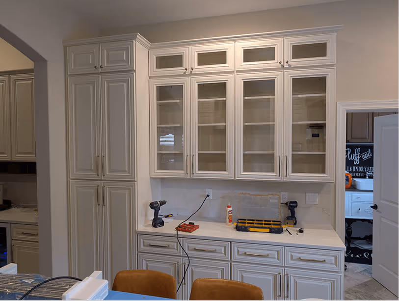 Floor-to-ceiling pantry tower with glass-door uppers and horizontal wine rack slots built into the bar station wall