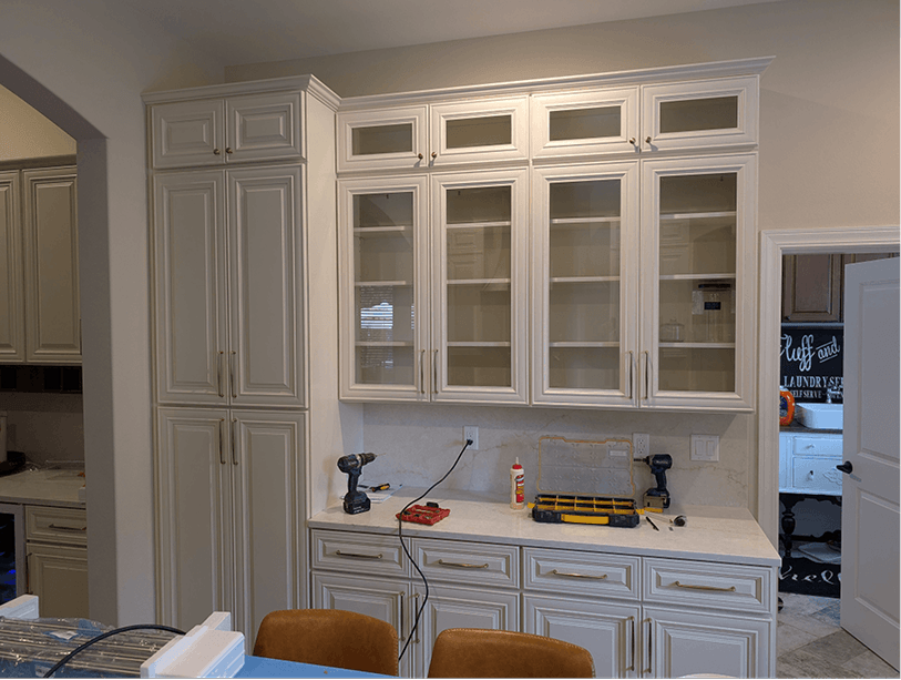 Floor-to-ceiling pantry tower with glass-door uppers and horizontal wine rack slots built into the bar station wall