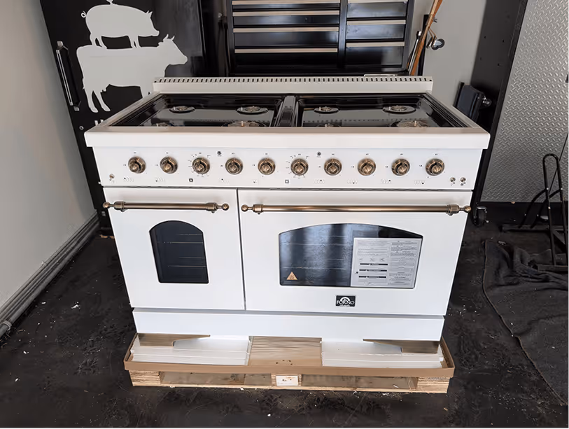 48-inch ILVE professional range on a shipping pallet with white enamel body, brass hardware, and six burners