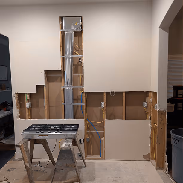 Range wall with electrical conduit and plumbing rough-in running vertically for the future pot filler