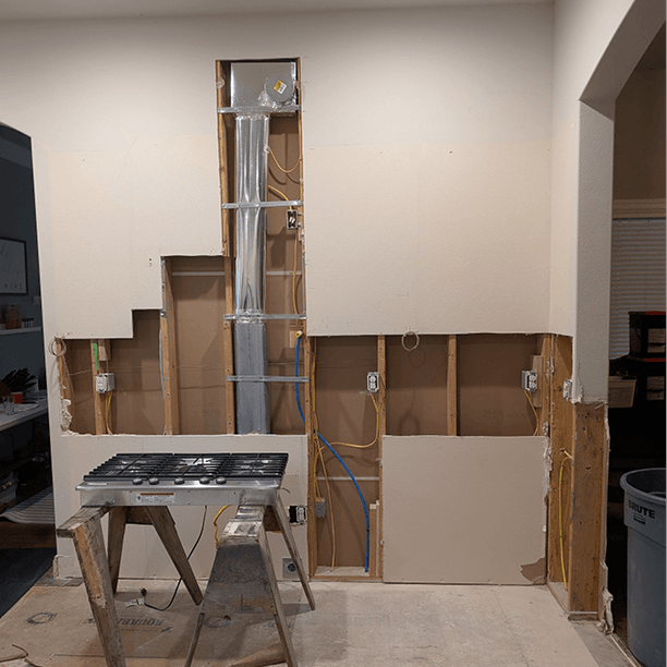 Range wall with electrical conduit and plumbing rough-in running vertically for the future pot filler