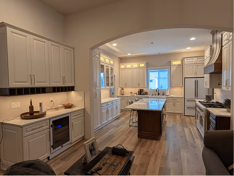 Finished kitchen viewed from the living room through the arched entry, wine fridge glowing at left, island centered in background