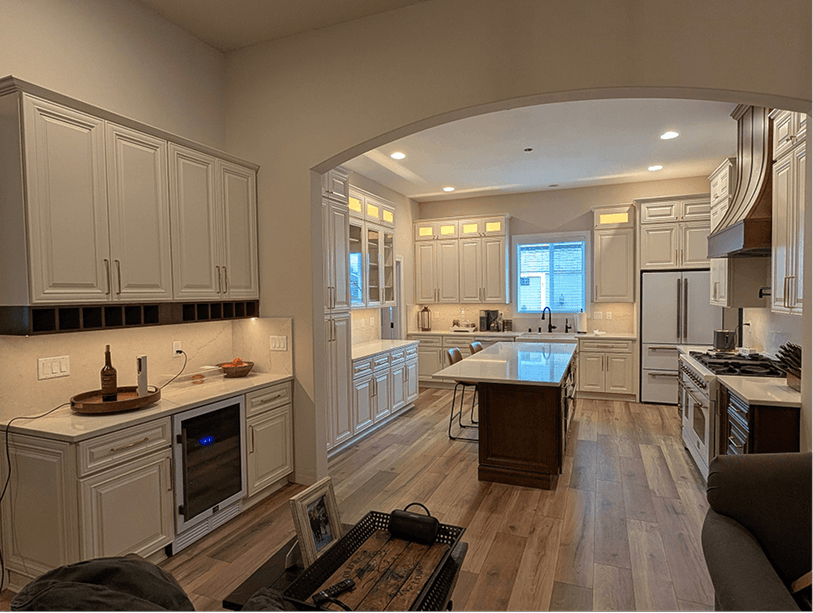 Finished kitchen viewed from the living room through the arched entry, wine fridge glowing at left, island centered in background