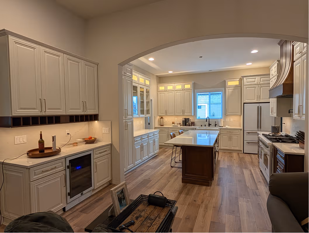 Finished kitchen viewed from the living room through the arched entry, wine fridge glowing at left, island centered in background