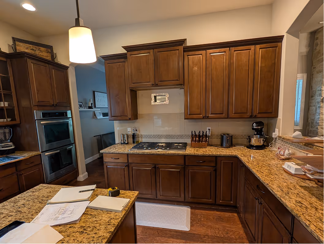 Cooking wall showing gas cooktop dropped into dark granite counter with double wall ovens on the right