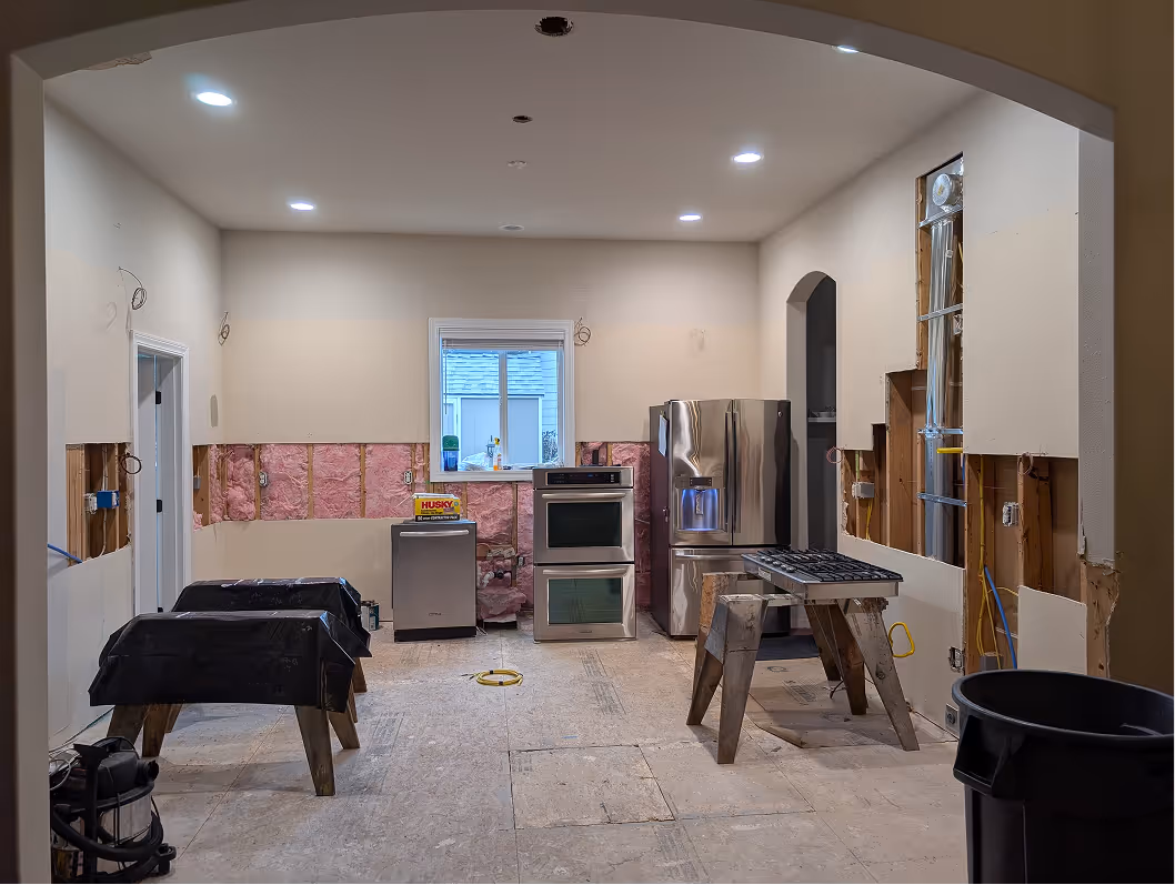 Kitchen stripped to bare walls and subfloor with new recessed lighting rough-ins visible in the ceiling